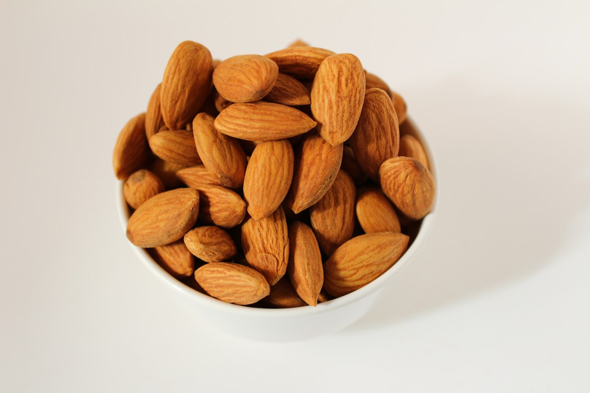 Almonds in a white bowl on a light surface.
